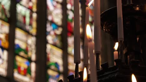 lit candles in front of colorful stained glass window