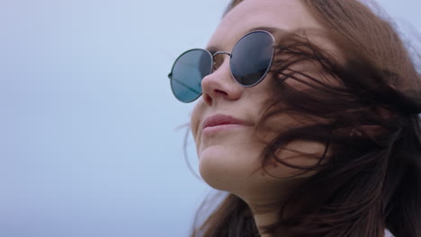 Retrato-De-Una-Hermosa-Mujer-Caucásica-Con-Gafas-De-Sol-Disfrutando-De-La-Tranquila-Playa-Al-Atardecer-Mirando-Contemplativamente-Corriendo-Con-La-Mano-Por-El-Cabello