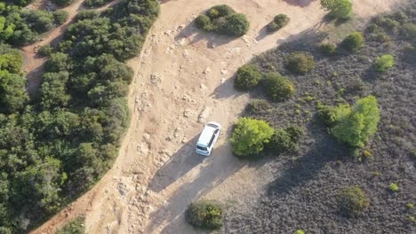 White-van-on-dirt-road-approaching-Fontainhas-Beach-in-south-Portugal-with-dogs-and-people-walking,-Aerial-top-view-follow-shot