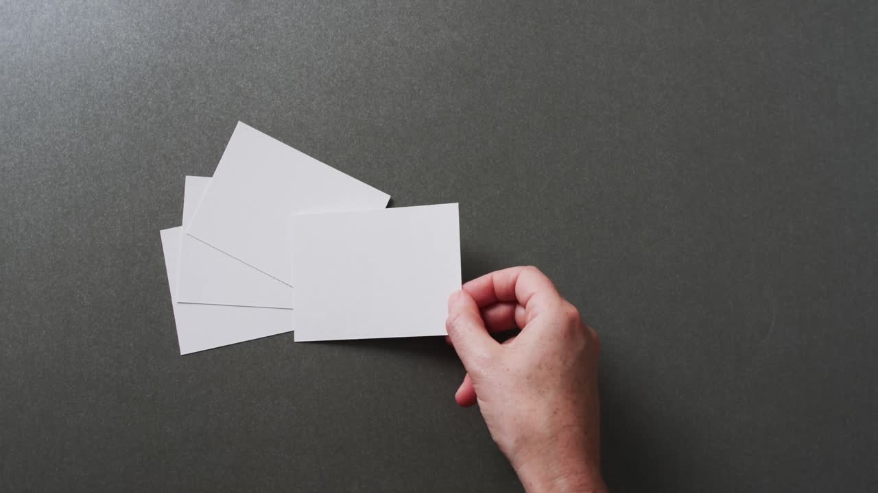 Mano che tiene un foglio di carta sopra altri fogli con spazio per il testo, su sfondo grigio, al rallentatore.