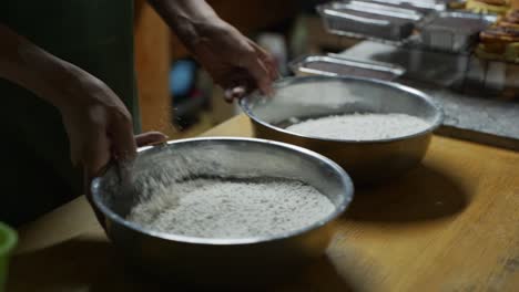 2 bowls of plain flour being sifted by hand on wooden kitchen tabletop, filmed as medium closeup slow motion shot