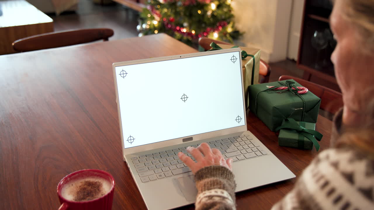 Senior woman using laptop at home, surrounded by Christmas gifts and tree