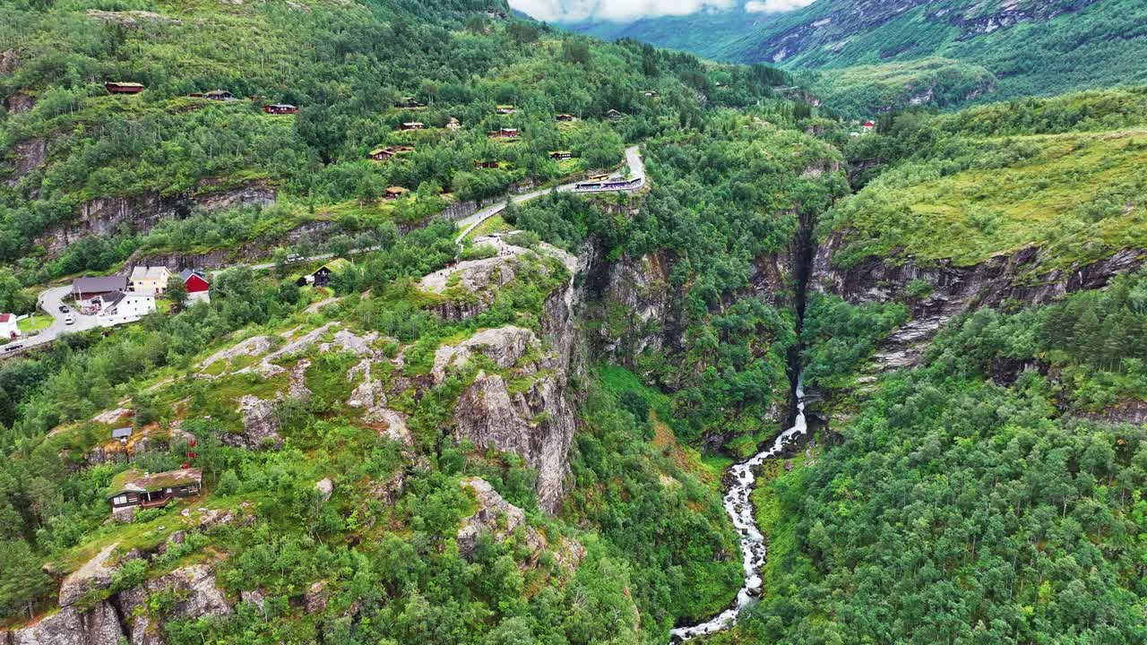 Letecký pohled na zelené kopce, kaňon a vyhlídkovou cestu nad vesnicí a fjordem Geiranger, Norsko.