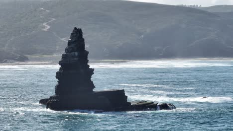 Aerial-shot-of-a-rock-jutting-out-of-the-water-in-a-beautiful-bay-on-a-sunny-day