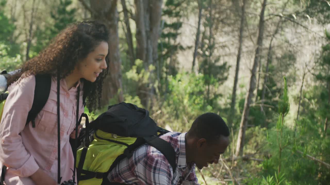 una pareja diversa sonriente tomando fotos con un teléfono inteligente y caminando por el campo
