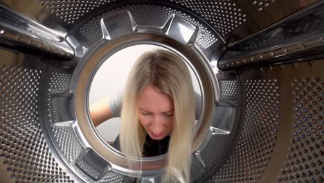 young beautiful blonde woman sneaks her head into washing machine.