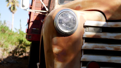 dropping down along the front of an old rusty vintage truck fender with glass headlight and grill in the sunlight