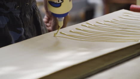 man squeezing tube of wood glue, spreading and applying onto wooden plank in workshop