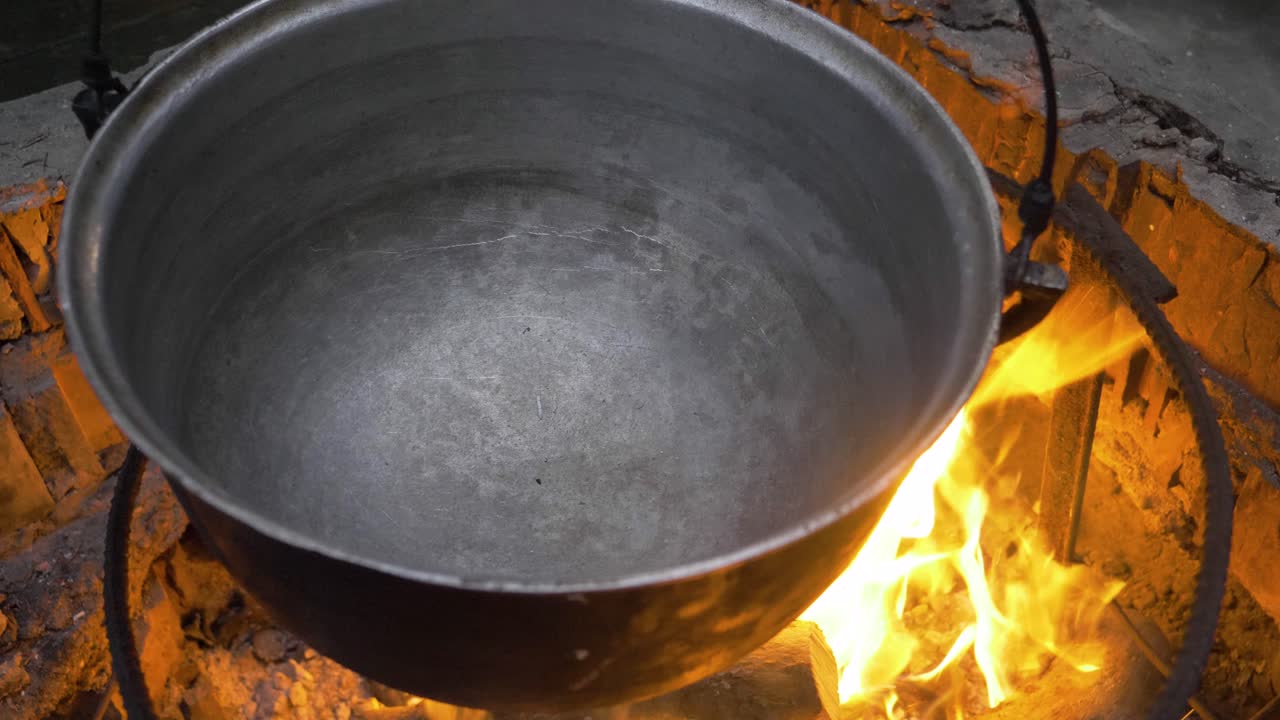 Black cauldron burning on the fire in nature near a cottage. The fire is very intense and bright red