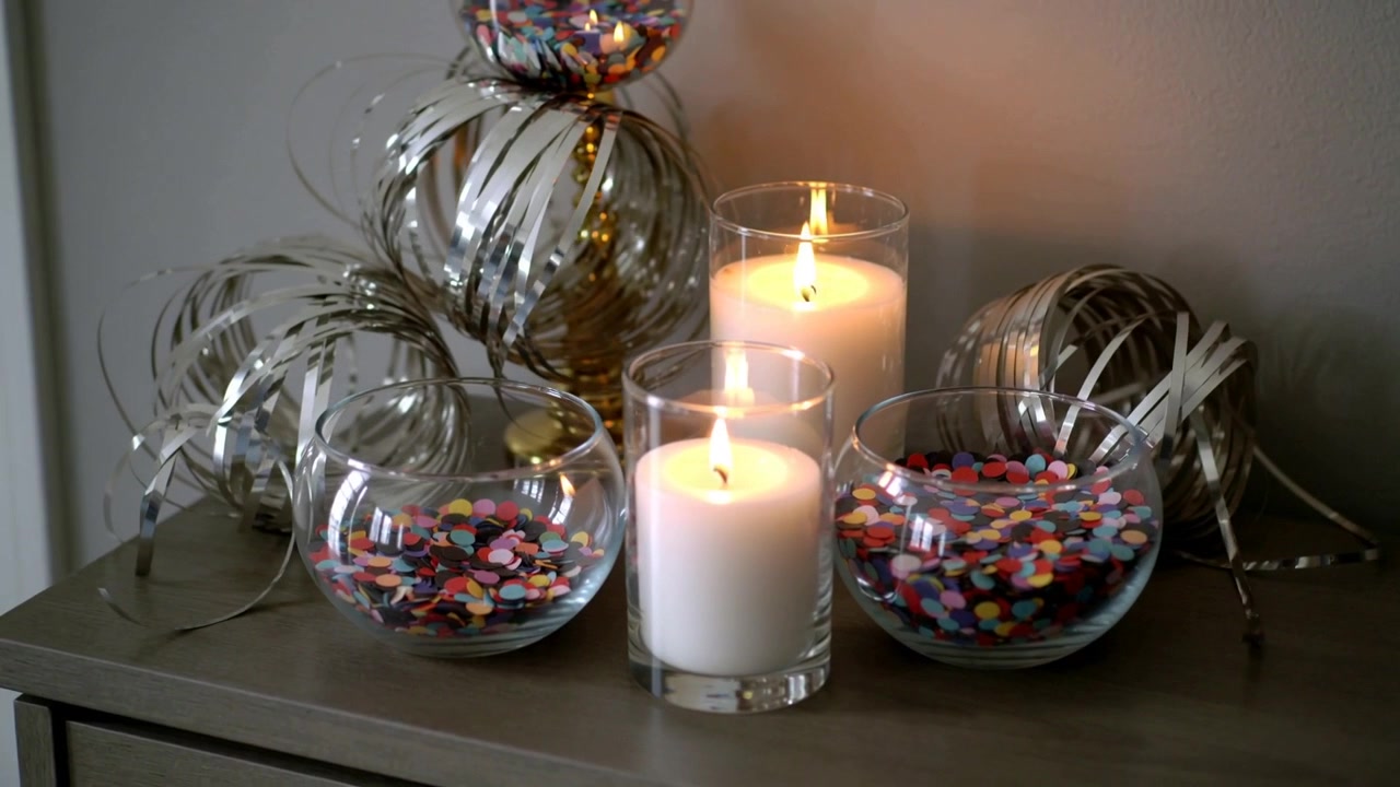 Câmera em movimento panorâmico filmando a decoração de mesa em um console, exibindo tigelas de confete e reflexos de velas acesas.