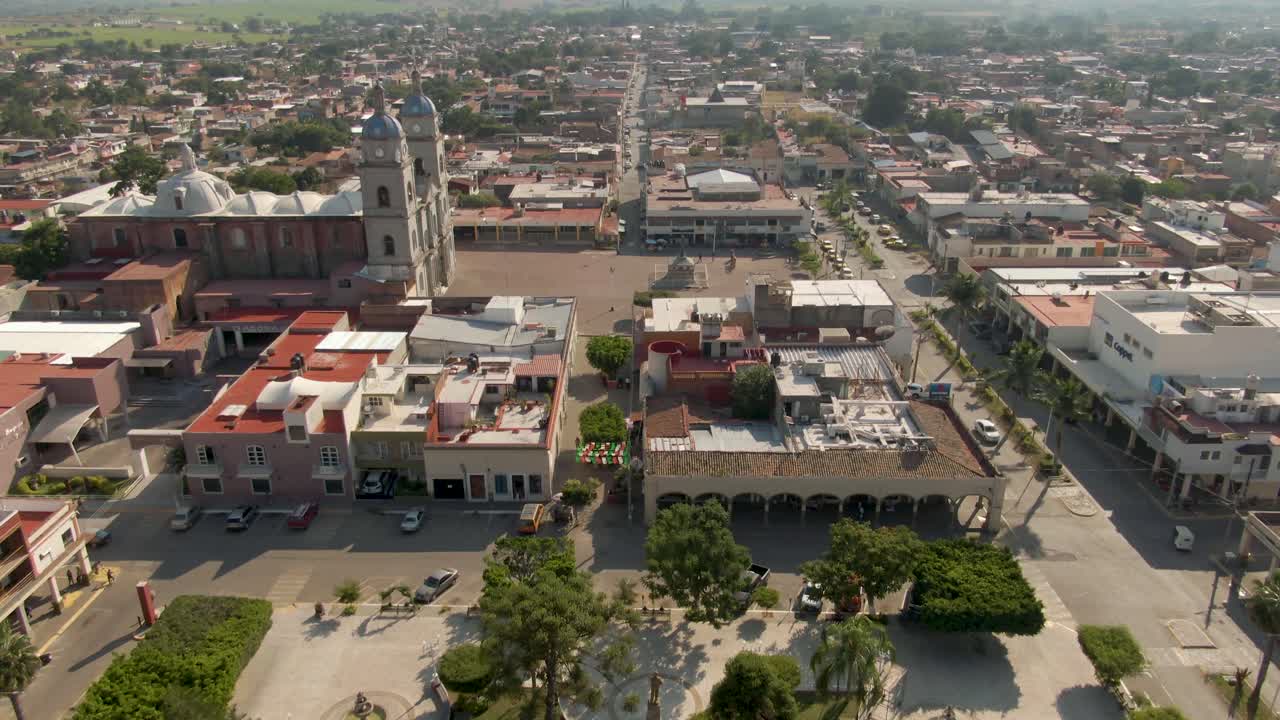Aerial top-down view of central park with white gazebo, tilt up reveals main church and public market in a small Mexican town