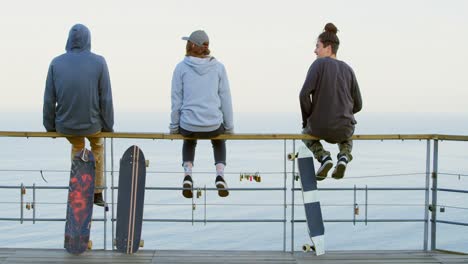 Rear-view-of-young-caucasian-skateboarder-with-skateboard-sitting-on-railing-at-observation-point-4k