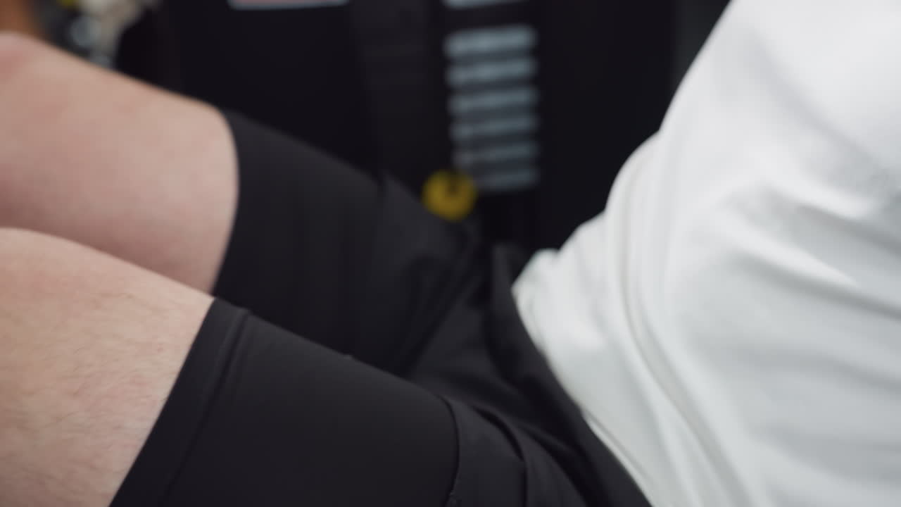 Gym enthusiast moves knee on leg press machine wearing black sports shorts under bright modern gym lighting, demonstrating controlled leg extension and focused strength training