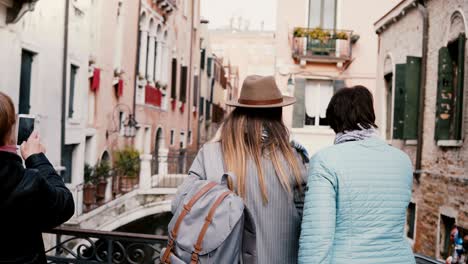 back view young daughter and senior mother stand together on canal bridge enjoying the view on vacation in venice italy.