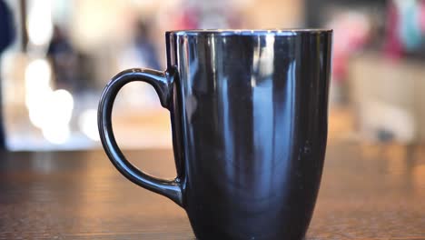 Clip-taken-at-coffee-shop-cafe-of-a-black-and-brown-coffee-cup-with-hot-coffee-or-tea-in-it,-as-people-shift-around-in-background