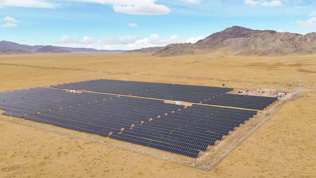 A wide aerial view of hundreds of solar panels in the desert of Uliastai, Mongolia. The drone glides around, showcasing the scale of the solar plant and its reach in this remote, barren landscape.