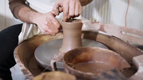 Close-Up-Of-Hands-Of-Man-Wearing-Apron-Working-At-Pottery-Wheel-Making-Vase-In-Ceramics-Studio