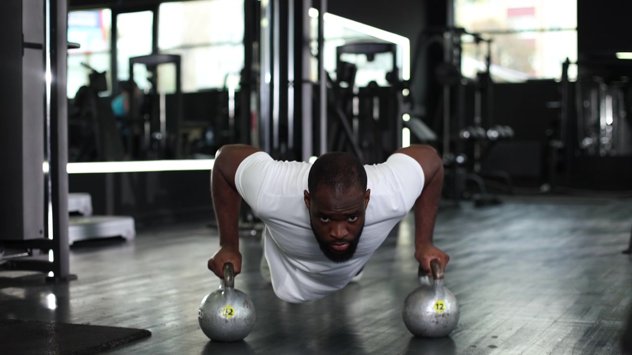 Uomo afroamericano muscoloso che esegue piegamenti con kettlebell in palestra