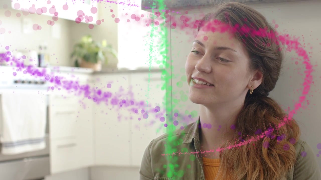 Donna seduta in cucina accanto a un mobile, particelle che si incurvano da sinistra attraverso il viso e disegnano un sorriso, effetto tecnologico.