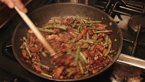 chef stirring vegan pork teriyaki with green beans and onion dish in frying pan