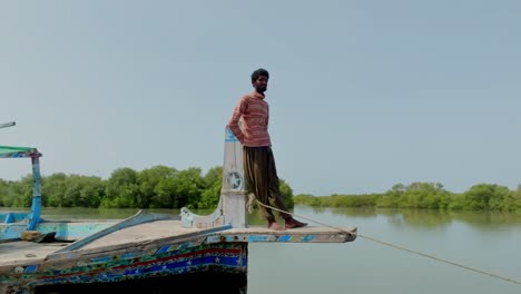 fisherman balances on the bow of a traditional boat navigating the serene waters of the indus river delta