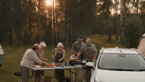 family cooking outdoors while camping in a forest at sunset