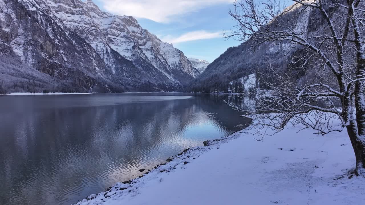 Drone flight over the snowy shores of Lake Klöntalersee on a typical winter day in the Swiss Alps, Canton of St. Gallen.