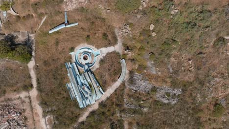 broken-down-water-slides-and-pools-in-dirty-dry-red-brown-landscape,-aerial