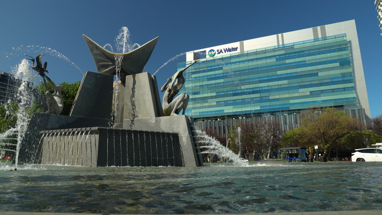 The SA Water building with a large, modern, artistic water fountain in the foreground. With themes of water conservation, city life, cost of living and architecture.