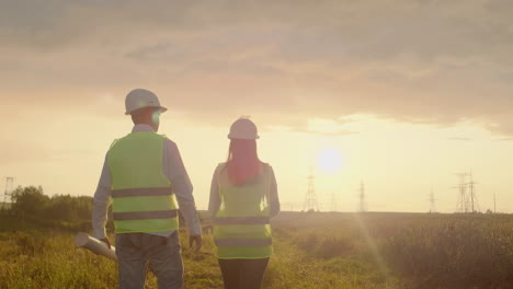 the view from the back: group of engineers at a high-voltage power plant with a tablet and drawings walk and discuss a plan for the supply of electricity to the city. transportation of renewable clean energy.