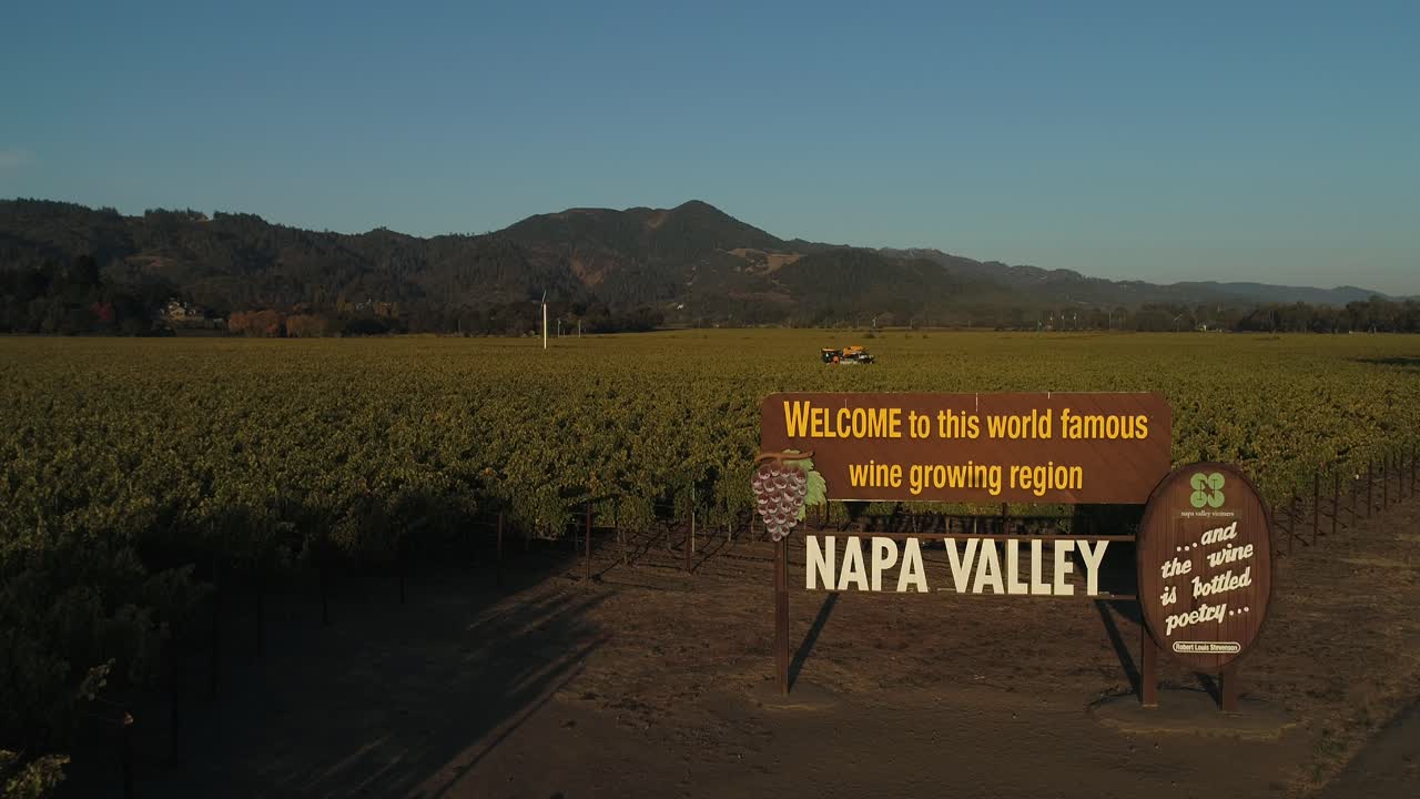 zoom in on Napa valley welcome sign with yellow vineyard vine trimmer tractor in vines