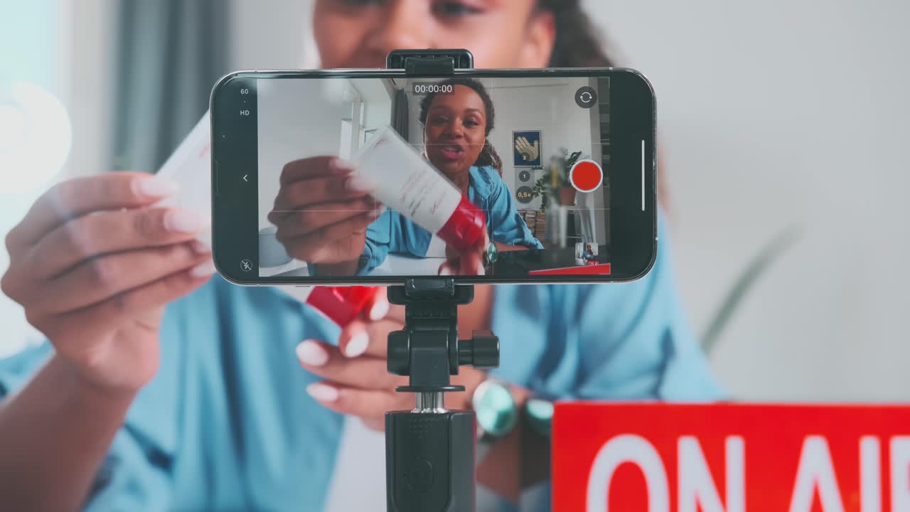Young energetic african american woman cosmetologist uses phone to shoot blog