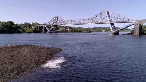 Toma-Aérea-De-Focas-Disfrutando-Del-Sol-Y-Luego-Chapoteando-En-El-Agua-Con-El-Puente-Connel-En-El-Fondo