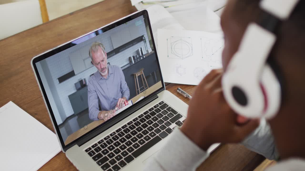 African american male college student holding notes while having a video call on laptop at home