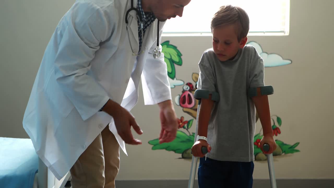 Male doctor assisting injured boy to walk with crutches