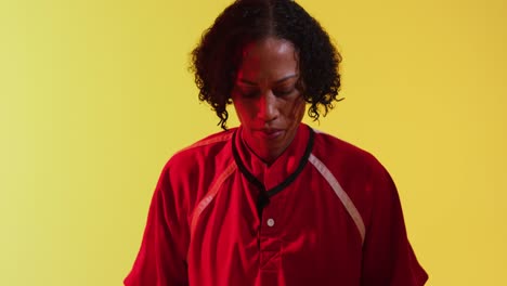 Portrait-of-african-american-female-rugby-player-with-rugby-ball-over-neon-yellow-lighting