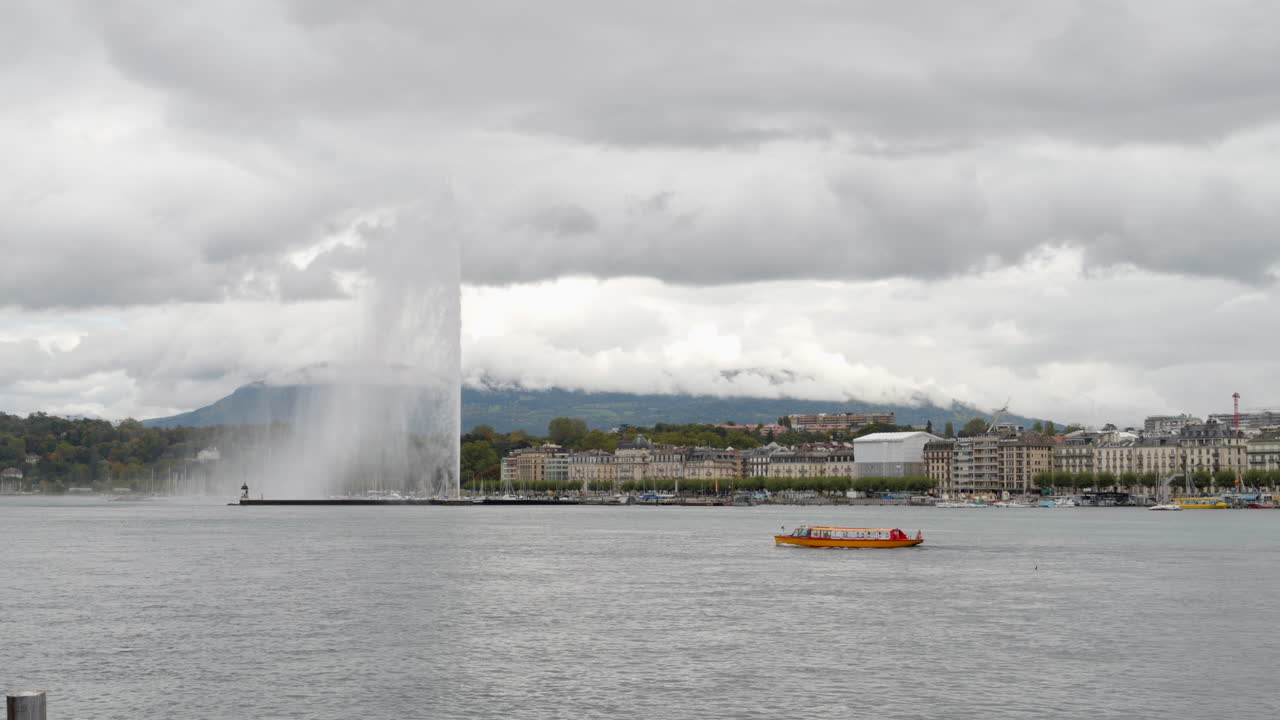 Yellow Taxi Boat on Lake Geneva with the Jet d'Eau and the Waterfront City on a Cloudy Day