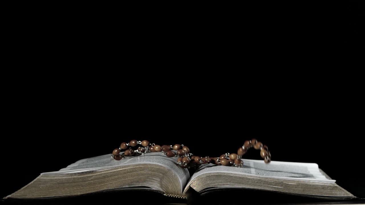 Grani del rosario che cadono su bibbia aperta su sfondo nero