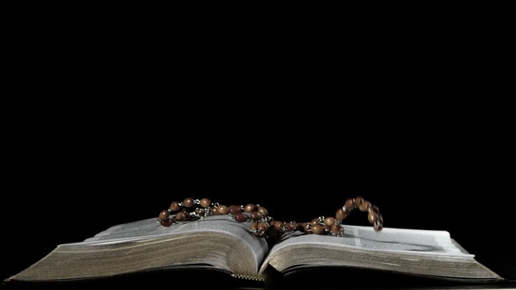 Rosary beads falling onto open bible on black background