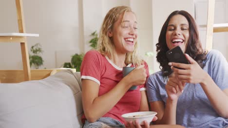 two young woman friends laughing together while looking in a smart phone