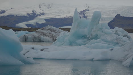 Glaciers-floating-in-Glacier-Lagoon,-Iceland,-with-seagulls-flying-overhead,-against-the-backdrop-of-blue-waters-moving-towards-Diamond-Beach