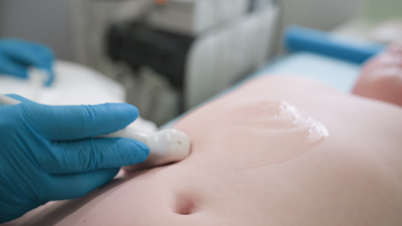Light skinned child lies on lab bed as lab scientist gently rolls ultrasound equipment over belly with visible gel, performing abdominal scan for medical analysis in clinical healthcare setting