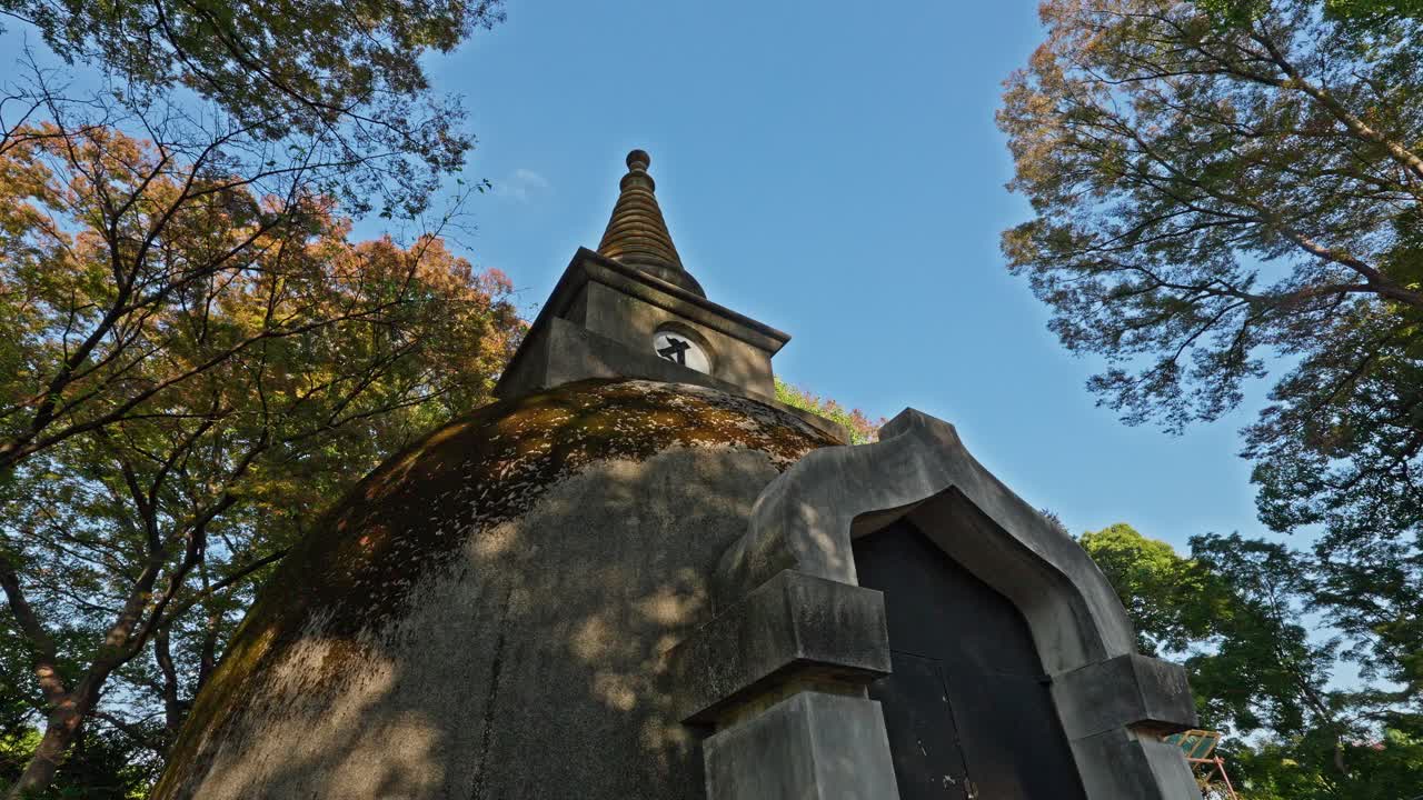 The weathered stone of the Ueno Pagoda is bathed in warm sunlight, surrounded by autumn trees in Tokyo's Ueno Park, a peaceful historical landmark.