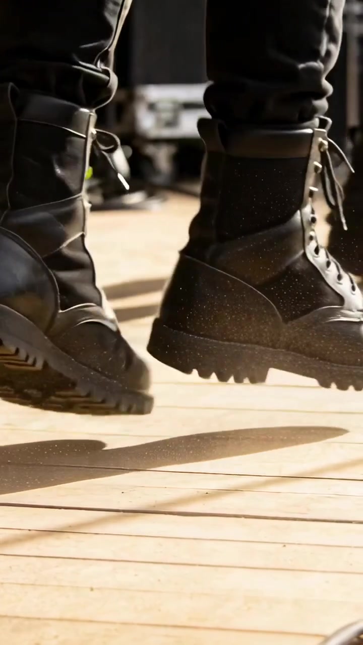 Musisi mengangkat kaki kiri dan menghentakkan sepatu bot, menekankan irama di atas panggung dengan debu yang terangkat