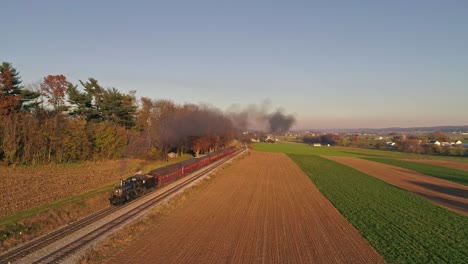 Luftaufnahme-Einer-Antiken-Dampflokomotive,-Die-Sich-Während-Der-Goldenen-Stunde-Am-Späten-Nachmittag-Mit-Personenwagen-Nähert-Und-Rauch-Und-Dampf-Bläst