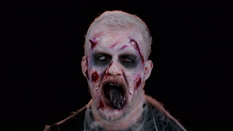 frightening scary man with halloween zombie bloody wounded makeup, showing tongue, trying to scare