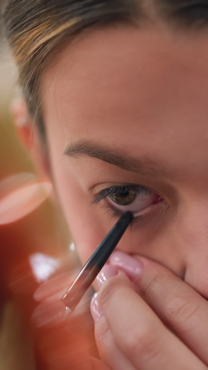Applying eyeliner during morning routine, Young woman carefully doing her makeup routine, Young girl with perfect manicure concentrating on her detailed beauty regimen in soft morning light