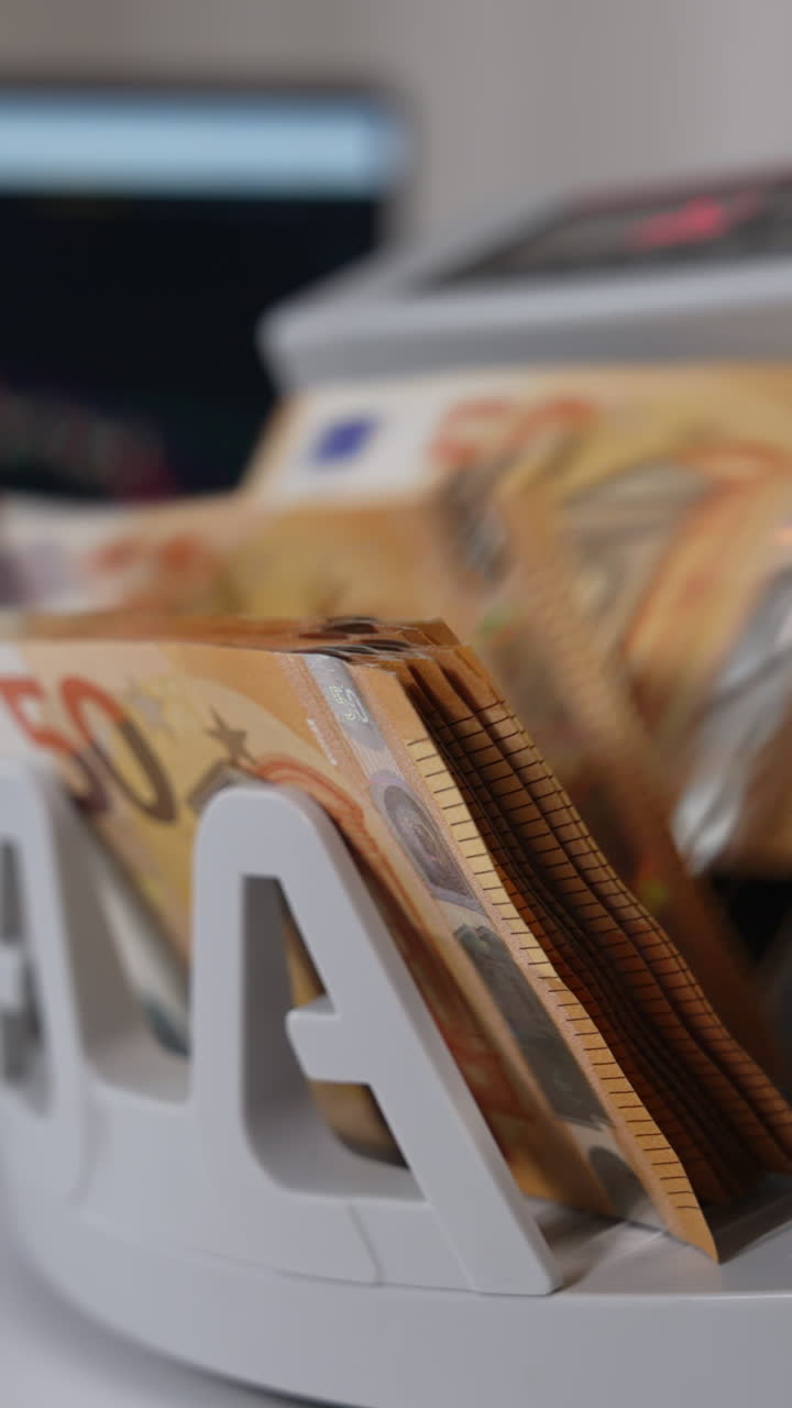 Working cash calculating equipment on the white table. Machine counting fifty euro banknotes. Laptop at backdrop. Vertical video