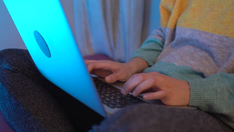 woman typing with the computer on top at night, she is sitting on the bed