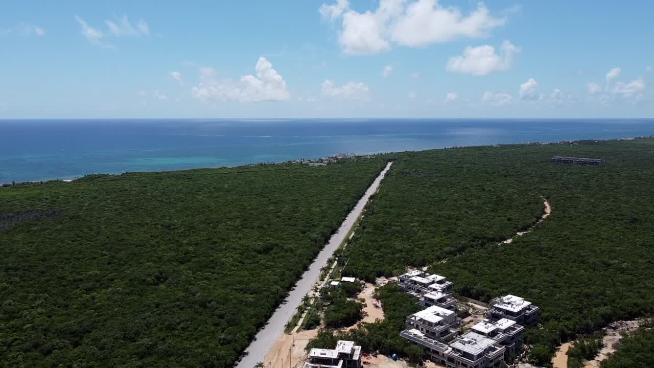 Empty road in Tulum surrounded by jungle leading to the coastline of Hotel Zone on sunny day, aerial